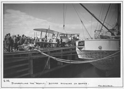 People watching a biplane being loaded onto a ship at a Melbourne dock. 