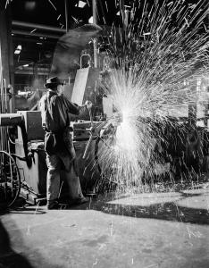 Sparks fly as a man operates a factory machine.