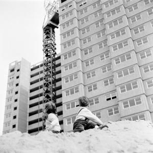 2 young children play on a pile of sand beneath an apartment block being contructed.