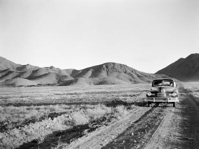 The photographers' car parked on a dirt road beside arid grassland. Mountain range in the background.