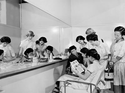 7 women viewing magazines while reflected in a mirror.