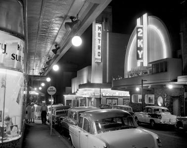 Night street view of pedestrians, parked cars, Metro Theatre and 2KY radio.