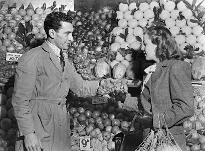 A grocer handing a woman a bag of mixed nuts.