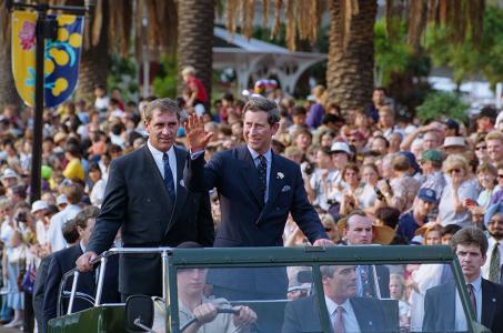 Prince Charles and John Fahey stand in the back of a Land Rover being driven by crowds.