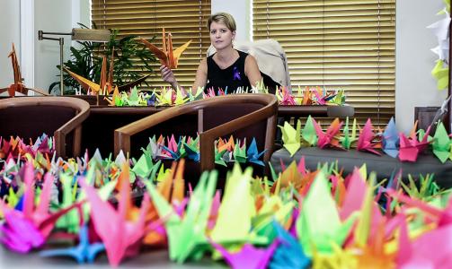 Natasha Scott Despoja sitting at her desk, surrounded by colourful paper cranes on all surfaces. 