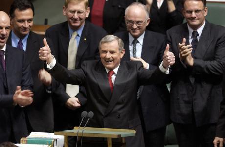 Simon Crean holding two thumbs up, standing behind a speaker's podium.