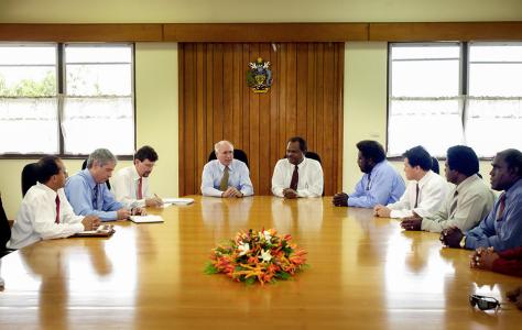 John Howard and Sir Allan Kemakeza sitting at the head of a table in the Solomon Islands. 