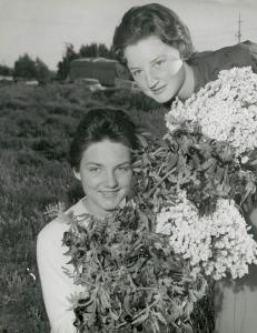 2 women each holding a bunch of wild-flowers pose for a photo.