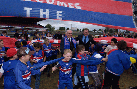 Donning a team scarf, Prime Minister John Howard and David Smorgon, Western Bulldogs football club president, celebrate the federal government’s $8-million funding pledge to save the club’s home ground, Whitten Oval, Footscray, Victoria, August 2004. NAA: A14482, 040483DI-0998. AUSPIC photographers: David Foote and Allan Porritt © Commonwealth of Australia, 2004