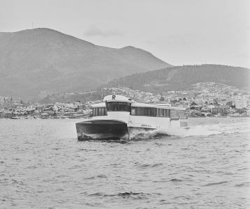 Catamaran on the ocean with buildings and mountains on the shore behind.