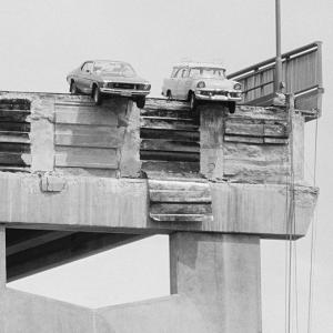 2 cars grounded on the edge of the bridge above the missing section.