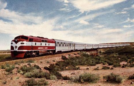 Red train locomotive with silver carriages in the desert.