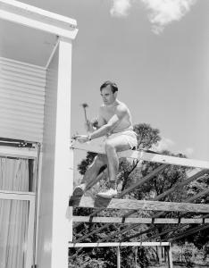 Jos Teunissen sits astride a rafter while hammering a nail.